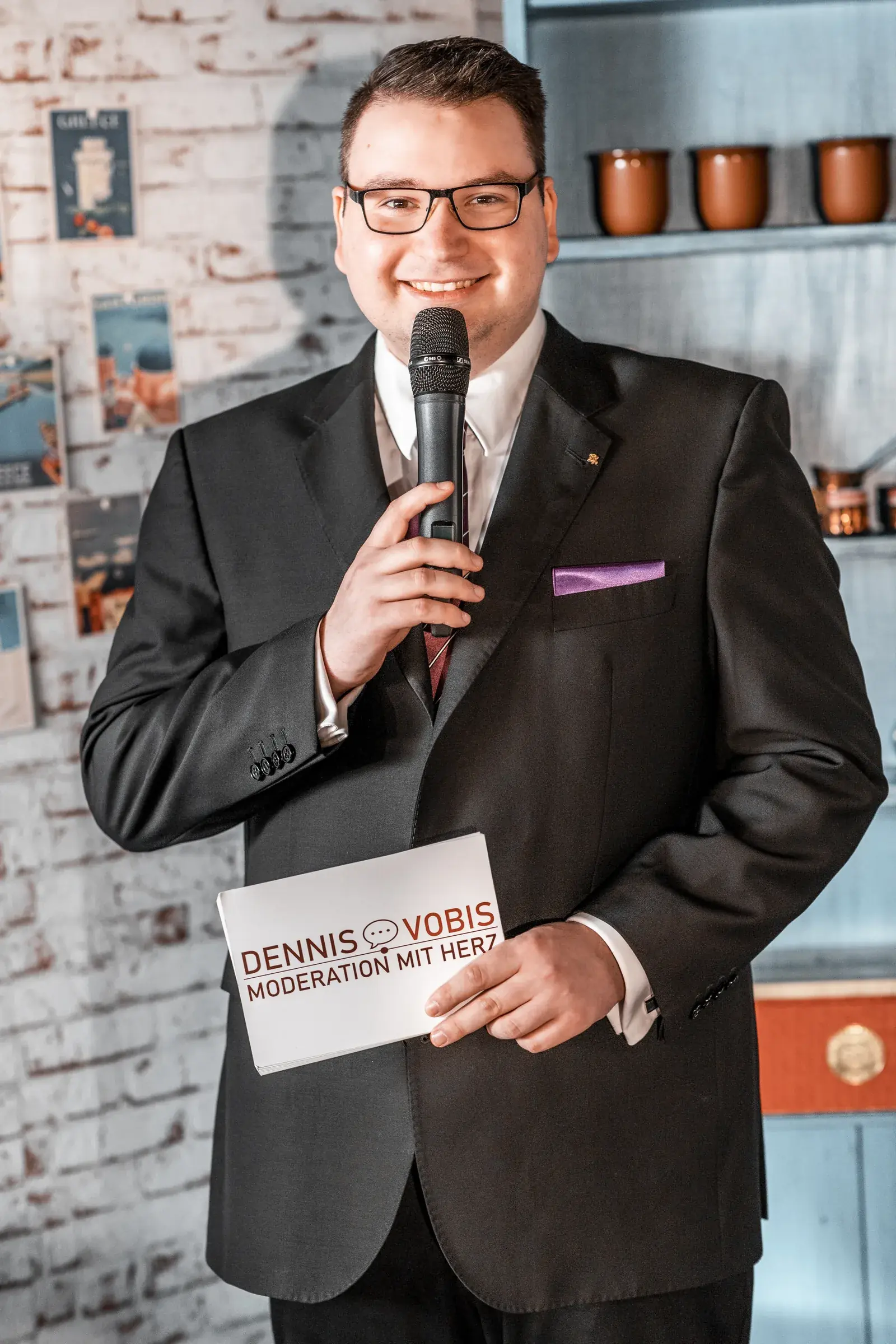 Dennis Vobis moderiert mit Mikrofon auf einer Bühne